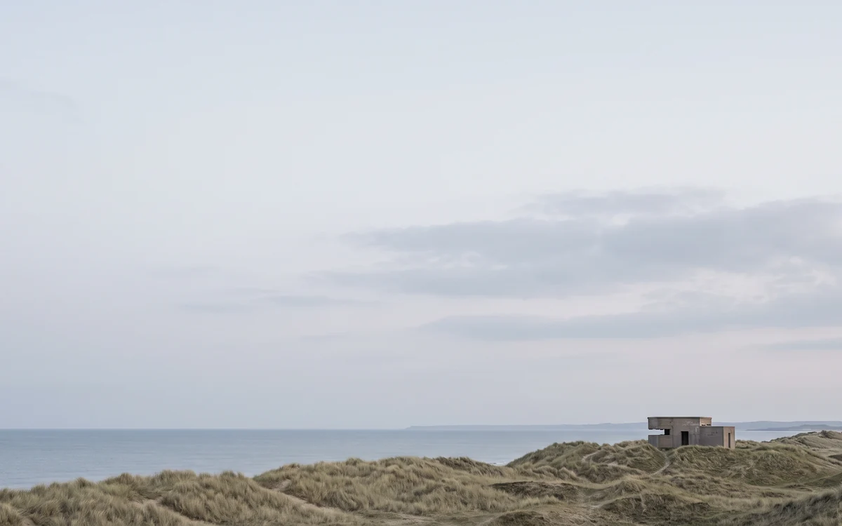 A low concrete building on grassy dunes above the sea at first light
